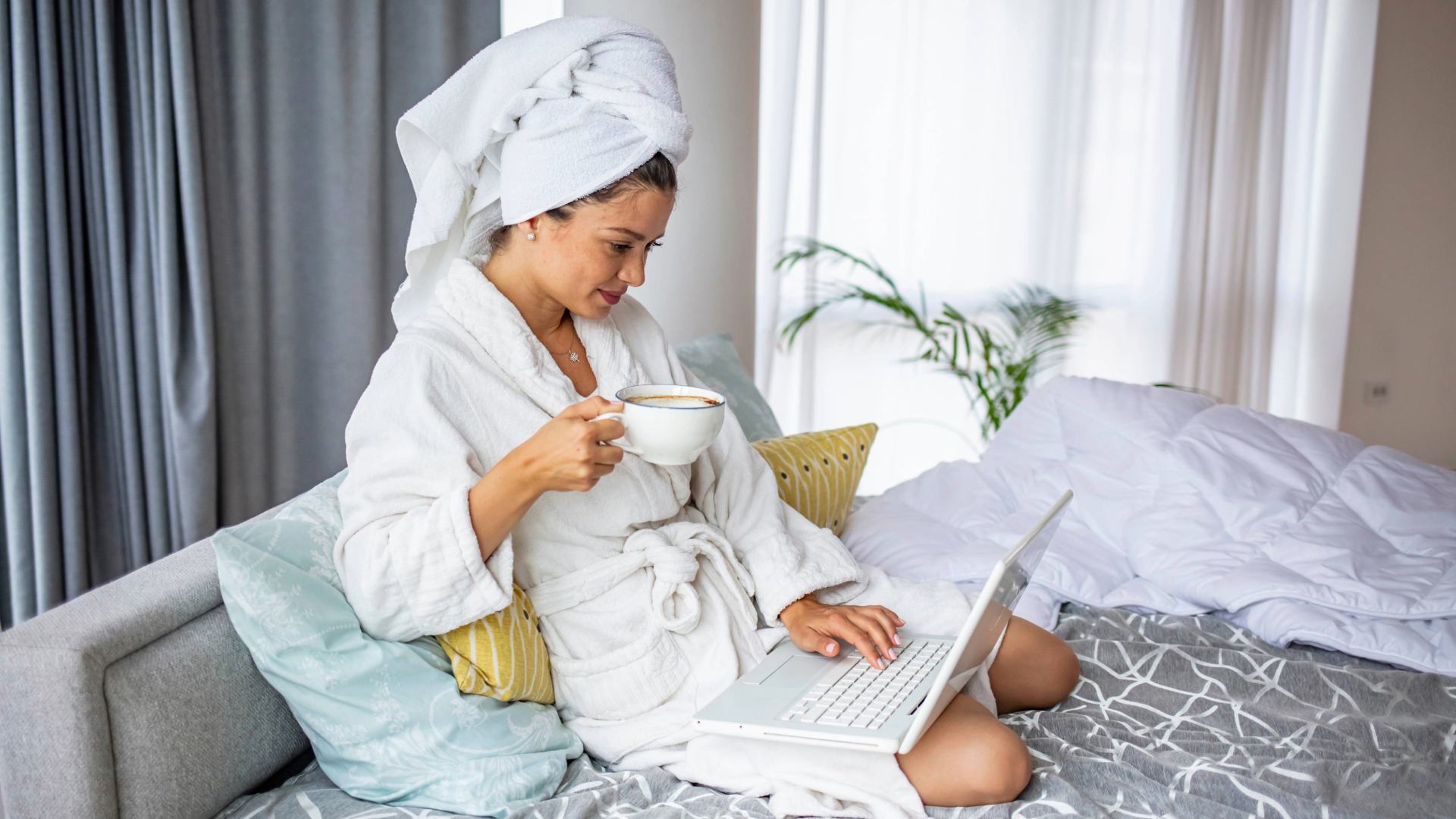 a lady looking happy and sipping coffee while sitting on a comfortable mattress